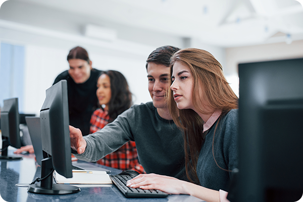 Analista explicando algo para jovem aprendiz em frente ao computador no escritório.