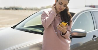 Mulher encostada no carro solicitando assistência 24 horas após uma pane elétrica no carro.