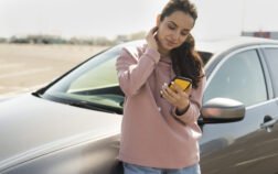 Mulher encostada no carro solicitando assistência 24 horas após uma pane elétrica no carro.