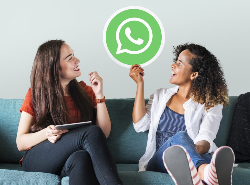 Mulheres sentadas no sofá segurando  na mão um ícone do username WhatsApp empresas.
