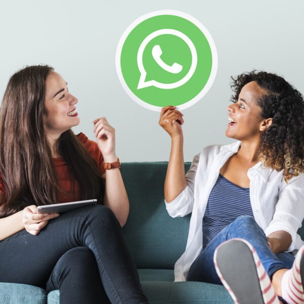 Mulheres sentadas no sofá segurando na mão um ícone do username WhatsApp empresas.